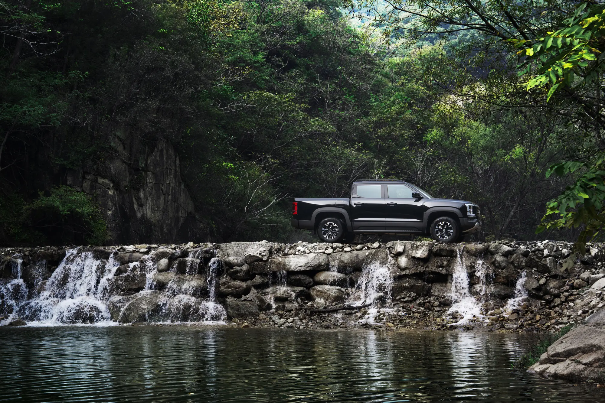 BYD Shark negro sobre un muro de piedra junto a una cascada