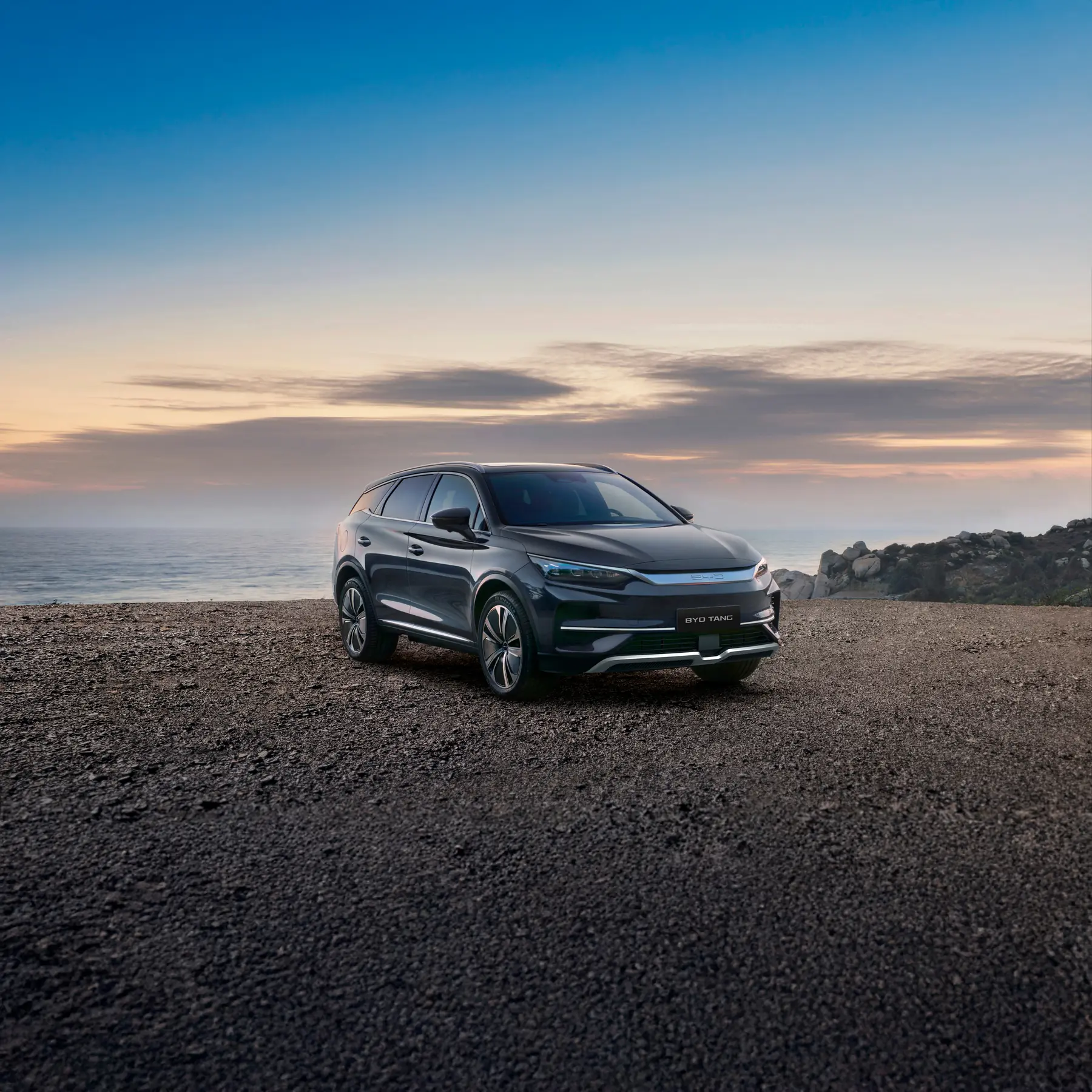 BYD Tang sobre una playa de piedra al atardecer